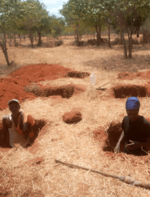 Two people sitting in a hole dug out of the ground.