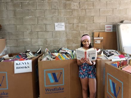 A girl standing in front of boxes with books.