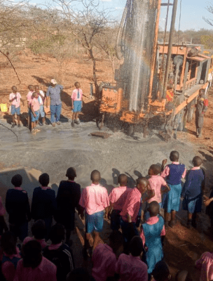 A group of people standing around in front of a drilling rig.